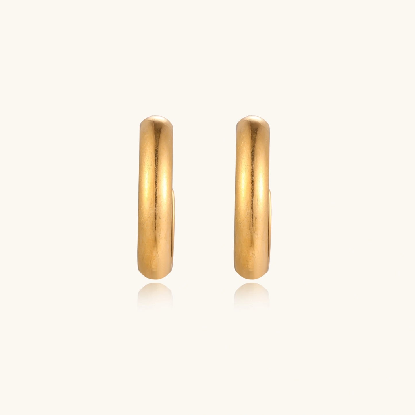 Chunky tubular hoop earrings in warm 14K gold-plated finish with smooth polished surface on cream background.